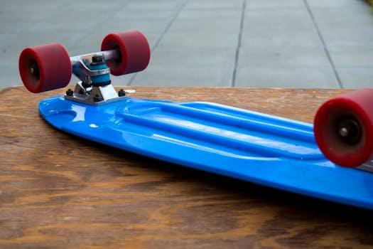 Close-up shot of a blue skateboard with red wheels on a wooden surface, outdoors.